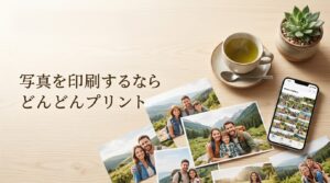 木目調のテーブルの上に置かれたスマートフォンとお茶、プリントされた複数の家族写真。「写真を印刷するならどんどんプリント」のアイキャッチ画像。